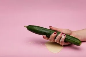 ladies hand holding a cucumber doused in cream