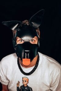 A man wearing a black dog mask with an orange tongue